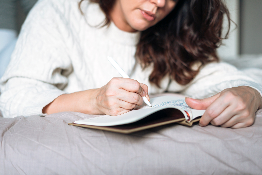 A woman lying on her bed writing in a journal