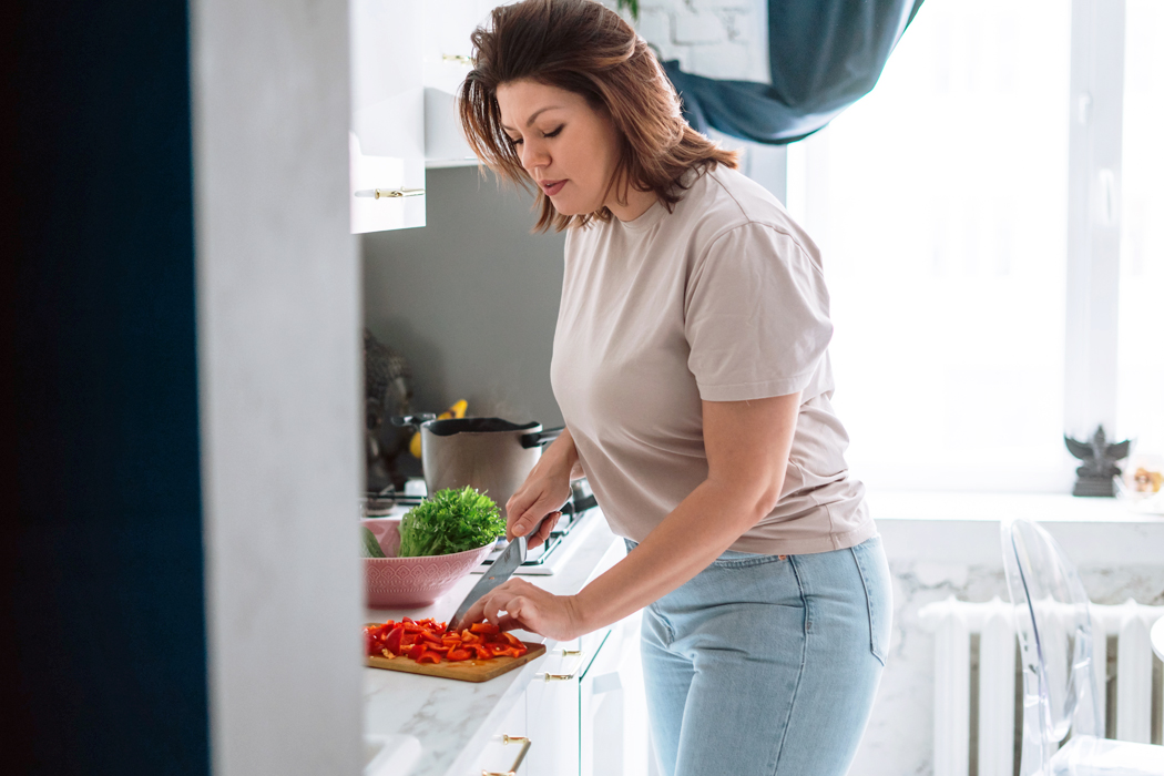 A woman cutting bright red vegetables in a well lit kitchen