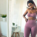 A woman in exercise clothes looking at her waist in the mirror