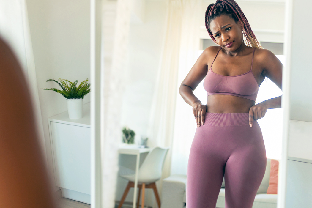 A woman in exercise clothes looking at her waist in the mirror