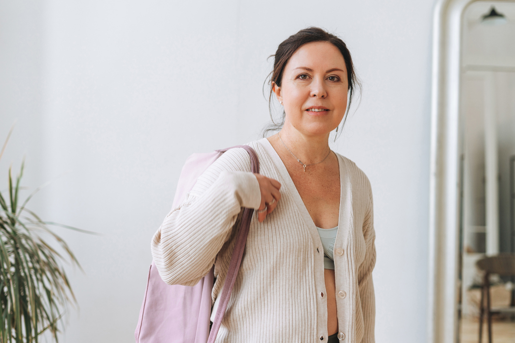 Middle aged woman dressed comfortably with a rolled up yoga mat slung over her shoulder