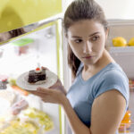 Young woman sneaking junk food from the refrigerator