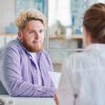 Man in purple shirt talking to a female doctor in an office setting