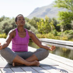 Woman sitting in a peaceful outdoor setting in a lotus pose