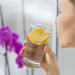 A young woman sipping a tall glass of water with fresh lemon slices