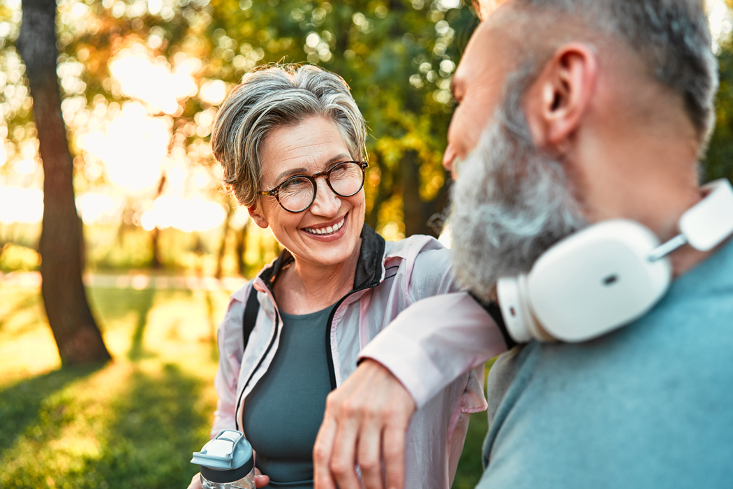 Healthy middle aged woman happily talking to middle aged man while walking outdoors