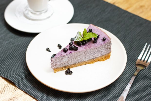 A slice of blueberry cheesecake with fresh berries and mint leaf