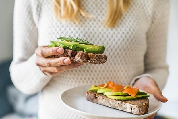 Woman holding a slice of freshly made avocado toast