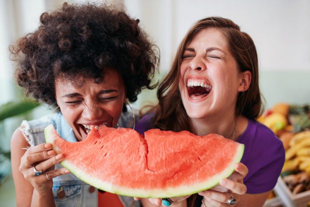 Two friends happily sharing a large slice of watermelon