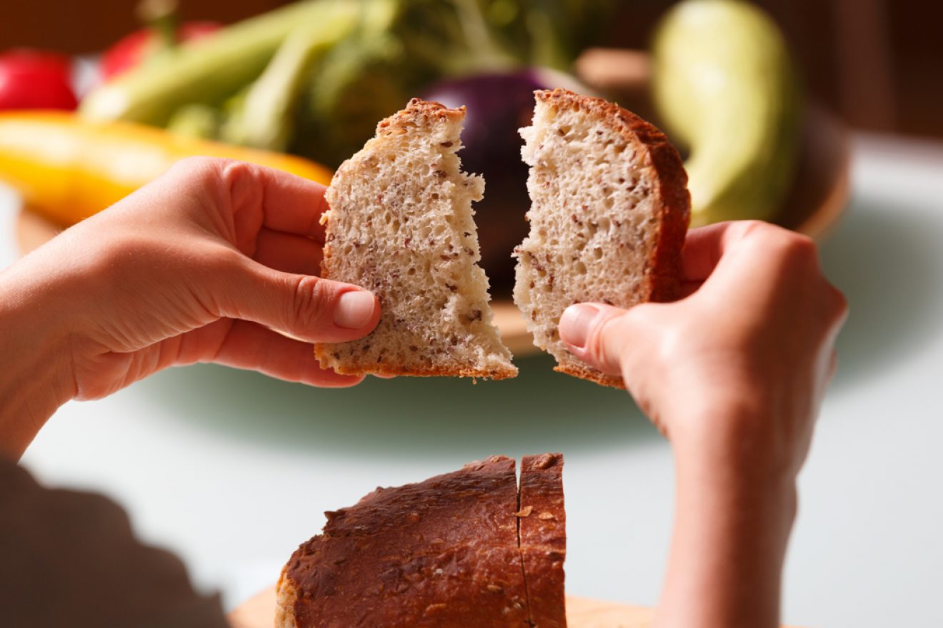 Two hands ripping a slice of fresh whole grain bread