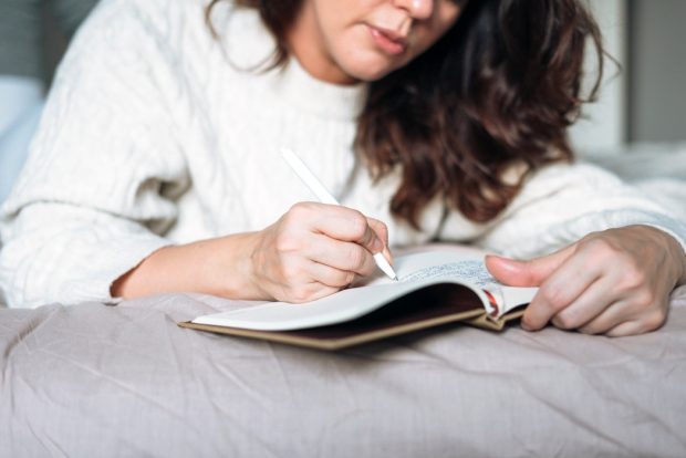 A woman lying on her bed writing in a journal