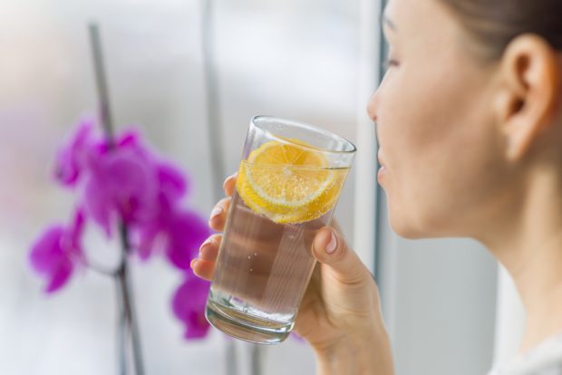 A young woman sipping a tall glass of water with fresh lemon slices