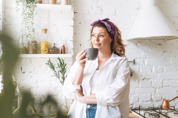 A woman sipping coffee in her brightly lit, modern kitchen
