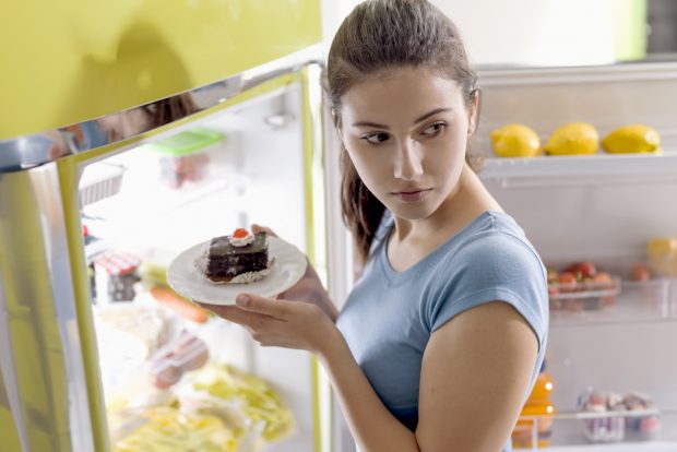 Young woman sneaking junk food from the refrigerator
