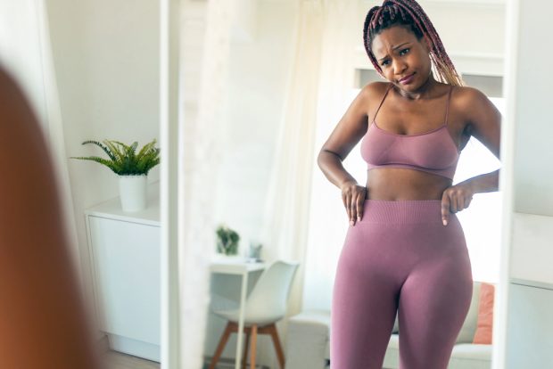 A woman in exercise clothes looking at her waist in the mirror