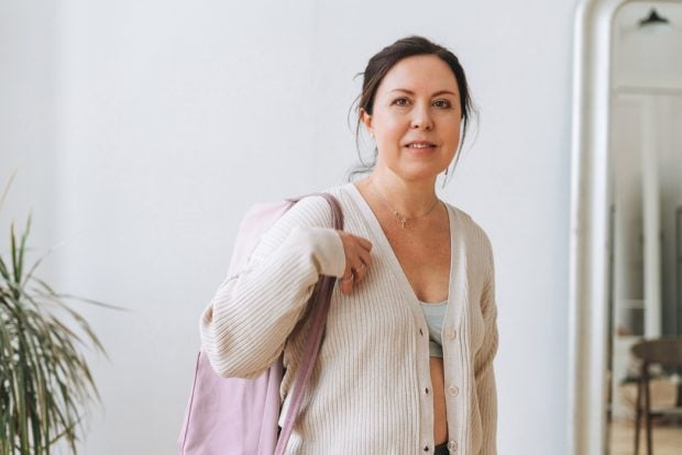 Middle aged woman dressed comfortably with a rolled up yoga mat slung over her shoulder